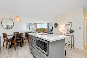 Cocina moderna con una isla central, comedor con sillas y vistas al exterior.