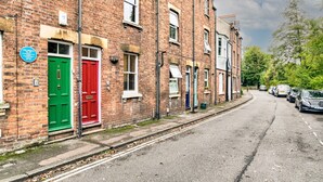 Une rangée de maisons mitoyennes aux portes vertes et rouges, une route dégagée et des voitures garées.