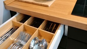 Una encimera de cocina con una tabla de cortar, un cuenco de tomates cherry, una planta de albahaca en maceta y un especiero.