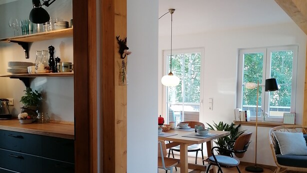 Una cocina moderna con vigas de madera, un comedor con mesa y sillas, y una sala de estar con sofá y ventana.