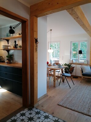 A modern kitchen with wooden beams, a dining area with a table and chairs, and a living space with a sofa and a window. - Woods: Accommodation **Haus im Glück** for large groups (St. Blasien)