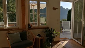 Una habitación acogedora con una silla de mimbre, una mesita con lámpara y una planta en maceta.