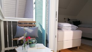 Una habitación acogedora con un banco de madera, una mesita con un libro y un florero, y una cama con almohadas.