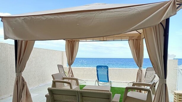 Un espace extérieur abrité, aménagé avec des meubles en osier et offrant une vue sur la mer.