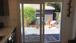 A kitchen with a sliding glass door leading to an outdoor patio area with a barbecue grill, chairs, and a small table. - The Bay Cabin, secluded retreat Freshwater Bay (Freshwater)