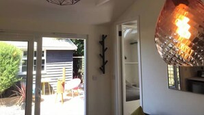 A room with a geometric pendant light, a large globe light, and a sliding glass door leading to an outdoor area with a patio and a building in the background. - The Bay Cabin, secluded retreat Freshwater Bay (Freshwater)