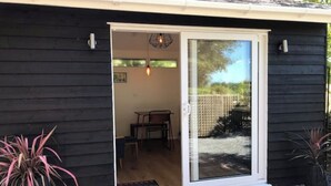 A dark wooden building with a sliding glass door leading to an interior space with a table and chairs. - The Bay Cabin, secluded retreat Freshwater Bay (Freshwater)