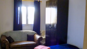 Una habitación con cama, sofá, armario y ventana con cortinas.