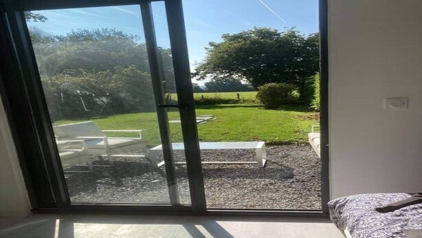 A room with a large sliding glass door leading to an outdoor area with a grassy lawn, a white bench, and a gravel path. - Nice apartment between Deauville and Pont-L'Evêque (Saint-Martin-aux-Chartrains)