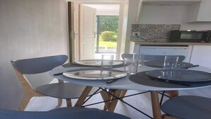 A dining area with a round table, four chairs, and a kitchen in the background. - Nice apartment between Deauville and Pont-L'Evêque (Saint-Martin-aux-Chartrains)