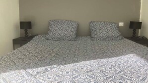 A bed with a patterned bedspread and two pillows, flanked by two bedside tables with lamps. - Nice apartment between Deauville and Pont-L'Evêque (Saint-Martin-aux-Chartrains)