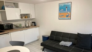 A compact living space with a kitchenette, a sofa, a dining table, and a poster on the wall. - Nice apartment between Deauville and Pont-L'Evêque (Saint-Martin-aux-Chartrains)