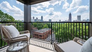 Un balcon agrémenté de meubles en osier, d’une table en verre et offrant une vue sur le panorama urbain.