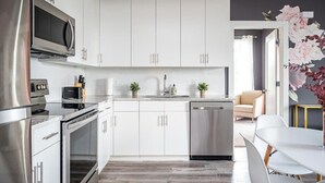 Une cuisine moderne avec des armoires blanches, des appareils en acier inoxydable et un coin repas comprenant une table et des chaises blanches.