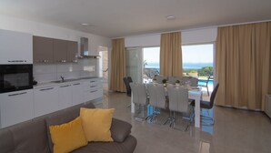 A modern kitchen with white cabinets, a built-in oven, and a dining area with a table and chairs.