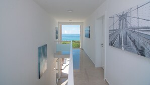A hallway with a view of the ocean, a staircase, and a large artwork on the wall.