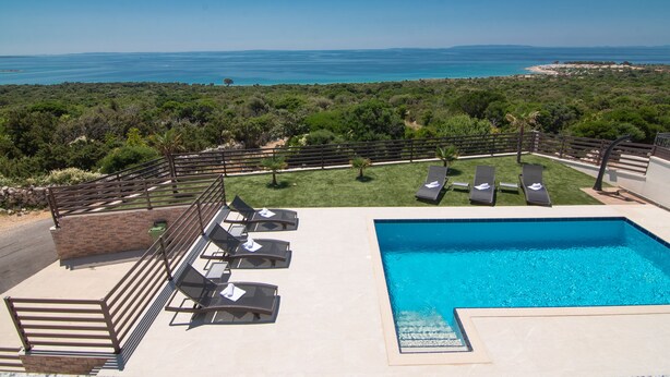 A pool area with lounge chairs and a view of the sea.