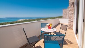A balcony with a table and chairs, overlooking a coastal landscape.