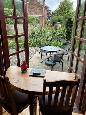 Une table en bois, entourée de chaises, et un vase rouge, le tout disposé dans une pièce dotée de grandes fenêtres donnant sur un jardin.