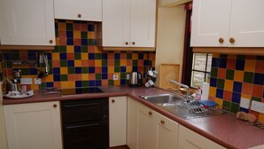 Una cocina con armarios blancos, un salpicadero de azulejos coloridos, un lavamanos de acero inoxidable y un taburete de madera.
