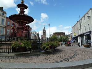 A public square with a central fountain, cobblestone pavement, and surrounding buildings including a bank. - Belmont Cottage -  a cottage that sleeps 3 guests  in 2 bedrooms (Dumfries)