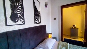 A bedroom with a large bed, a nightstand, a wall-mounted light, and a door leading to another room.