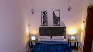 A bedroom with a large bed, two wall-mounted lamps, and two zebra-themed wall art pieces.