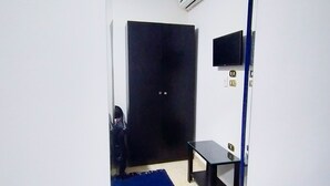 A room with a large mirror, a black wardrobe, a small table, and a mounted TV.