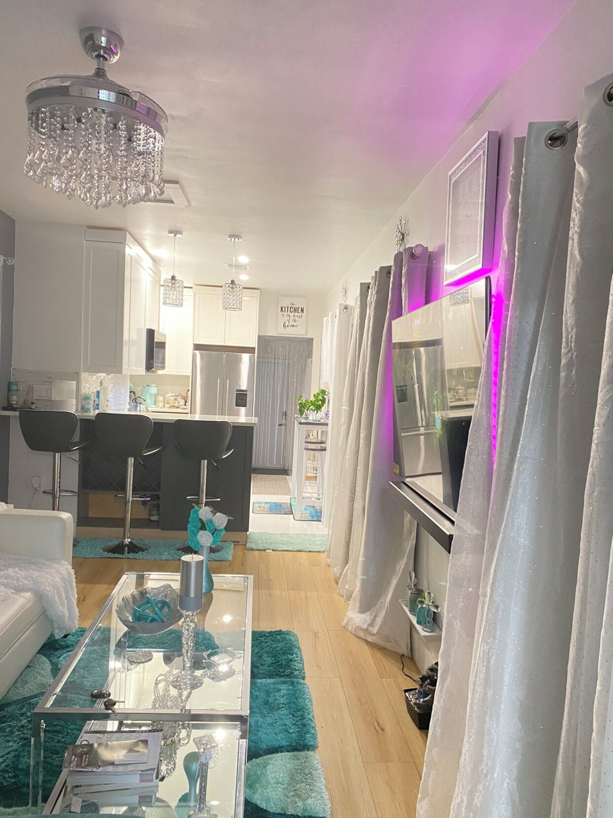 Un salon moderne avec une table basse en verre, des poufs turquoise et un lustre.