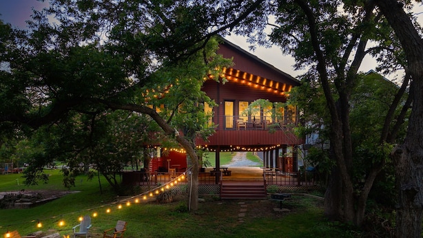 Uma casa de dois andares com área externa coberta, luzes de Natal e área de estar ao ar livre.