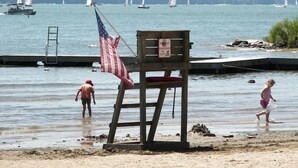A lifeguard chair with an American flag, a sandy beach, and sailboats in the background. - Wally`s House   |Kayaks|Firepit|Game Shed|Central! (Hawley)