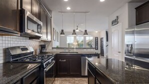 A modern kitchen with stainless steel appliances, dark cabinetry, and a tiled backsplash.
