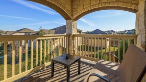 A covered balcony with stone arches, a table, and a chair, overlooking a residential area.