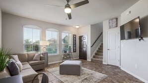 A spacious living room with a ceiling fan, a gray sofa, a coffee table, and a staircase leading to the upper floor.