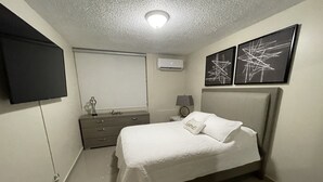 Una camera da letto con un letto, una cassettiera, un comodino, una lampada, una TV a muro e due quadri astratti.