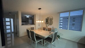 Un'area pranzo con un tavolo rettangolare, sei sedie, un lampadario e una finestra con persiane.
