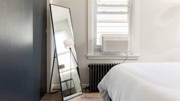 A bedroom with a large mirror, a radiator, and a window with blinds.