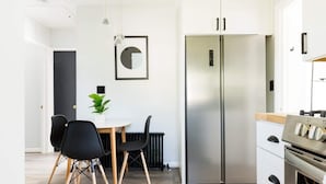 Een moderne keuken met een roestvrijstalen koelkast, een eettafel met stoelen en een potplante.