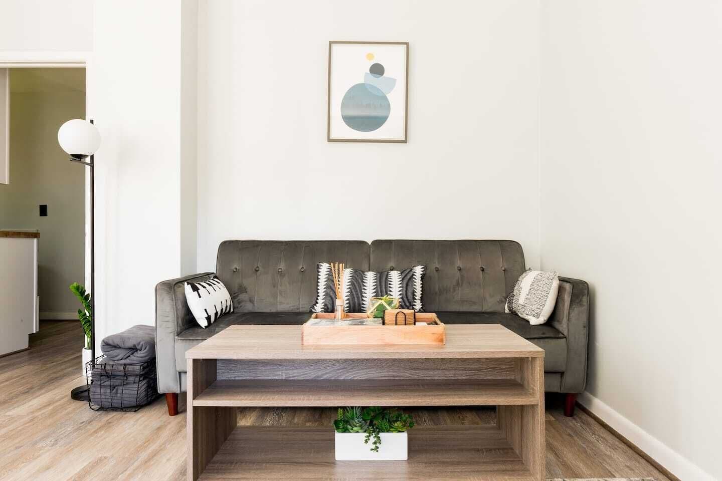 Una sala de estar con un sofá gris, una mesa de centro de madera y un cuadro abstracto enmarcado en la pared.