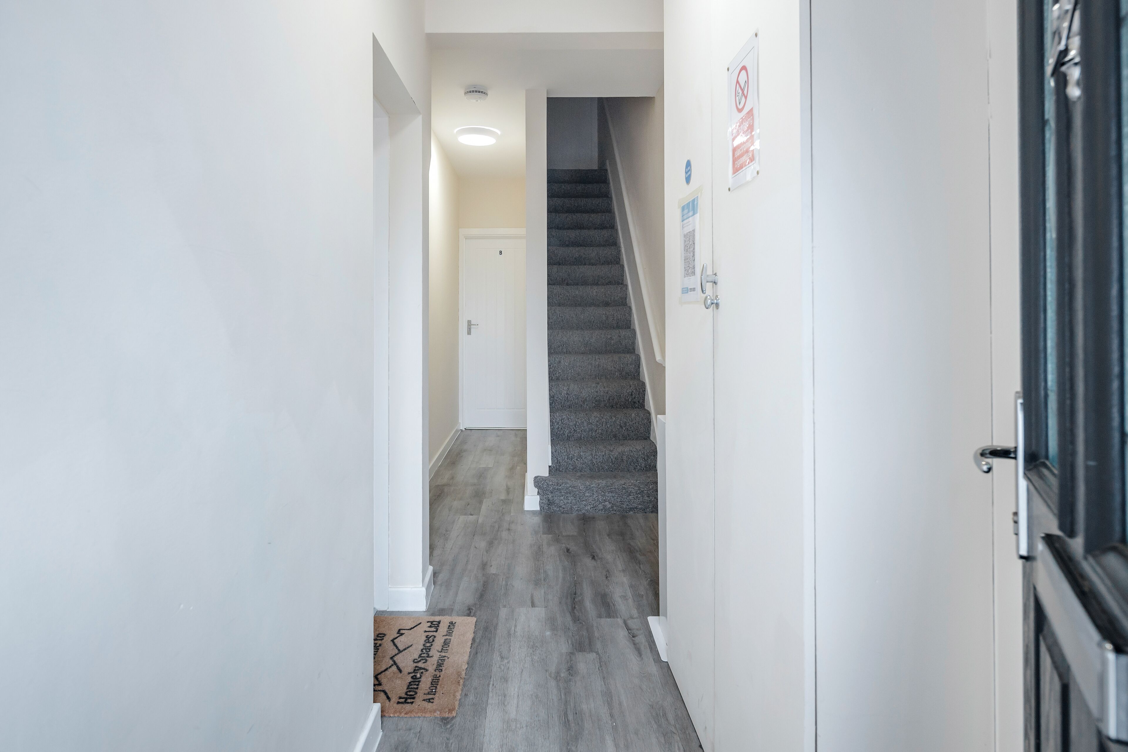 A hallway with a carpeted staircase, white walls, and a door at the end.