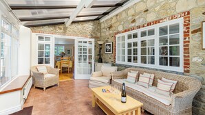 A cozy living room with wicker furniture, a stone wall, and large windows. - Rookley Farm Lodge (Rookley)