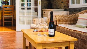A wooden table with a bottle of Prosecco and three glasses on it, in a room with a wicker sofa and a stone wall. - Rookley Farm Lodge (Rookley)