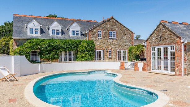 A swimming pool with a curved edge, surrounded by a paved area. - Rookley Farm Lodge (Rookley)