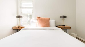 A minimalist bedroom with a large bed, two bedside tables with lamps, and a window with blinds. - Dog-Friendly Hudson Valley Escape with Hot Tub & Jacuzzi (Kingston)