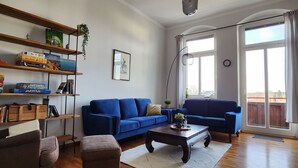 Una sala de estar con un sofá azul, una mesa de centro, piso de madera y una estantería con juegos de mesa.