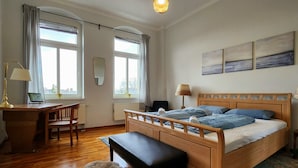 Un dormitorio con una cama de madera, un escritorio, una silla, un banco y un ventanal con cortinas.