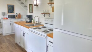 Une cuisine compacte avec des appareils électroménagers blancs, un plan de travail en bois et une petite étagère ornée d’une plante.