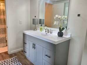 Een badkamer met een witte wastafel, een spiegel, een handdoekhouder en een orchidee in pot.