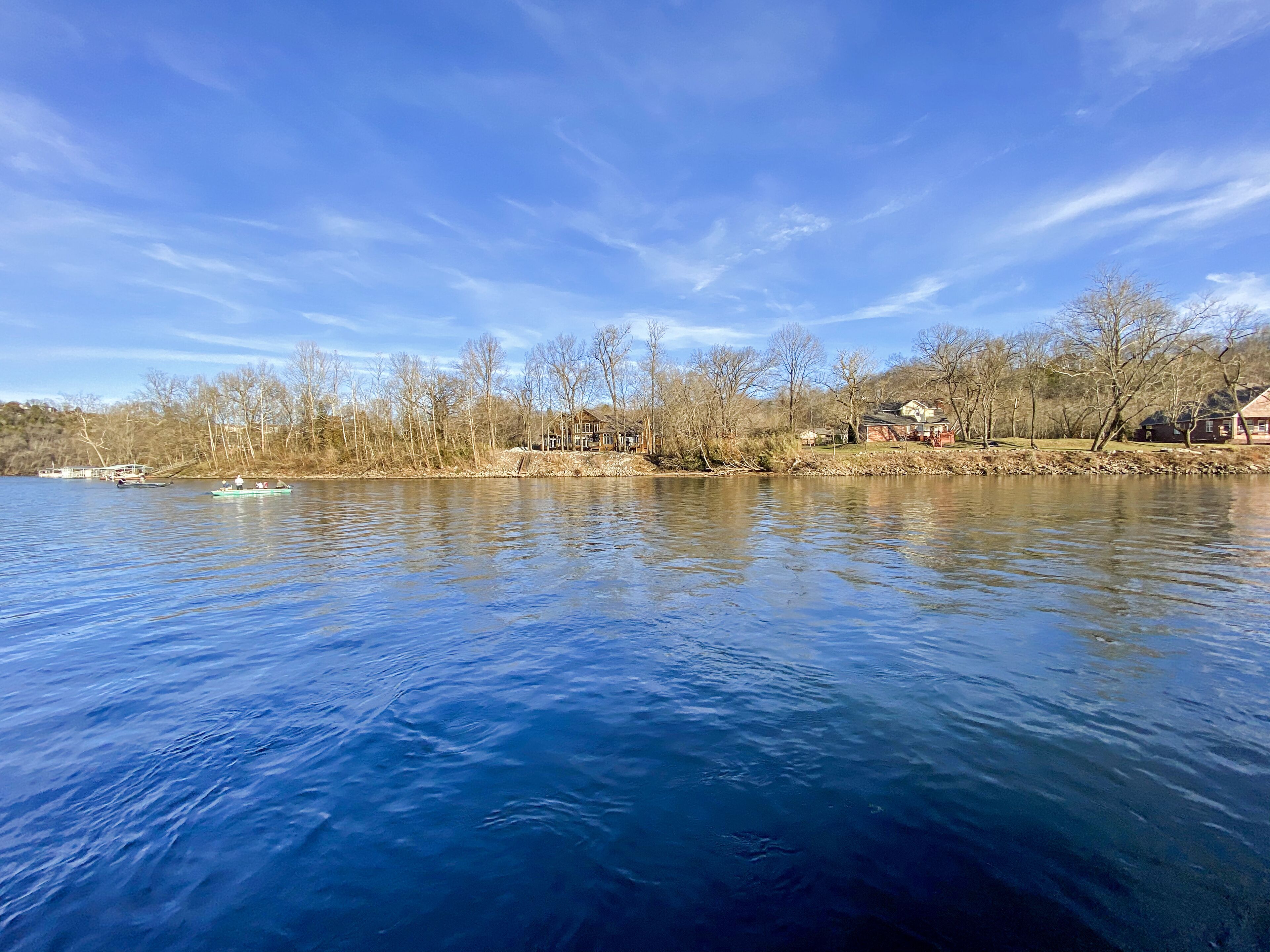 Une rivière paisible, bordée de bateaux, d’arbres et de maisons.