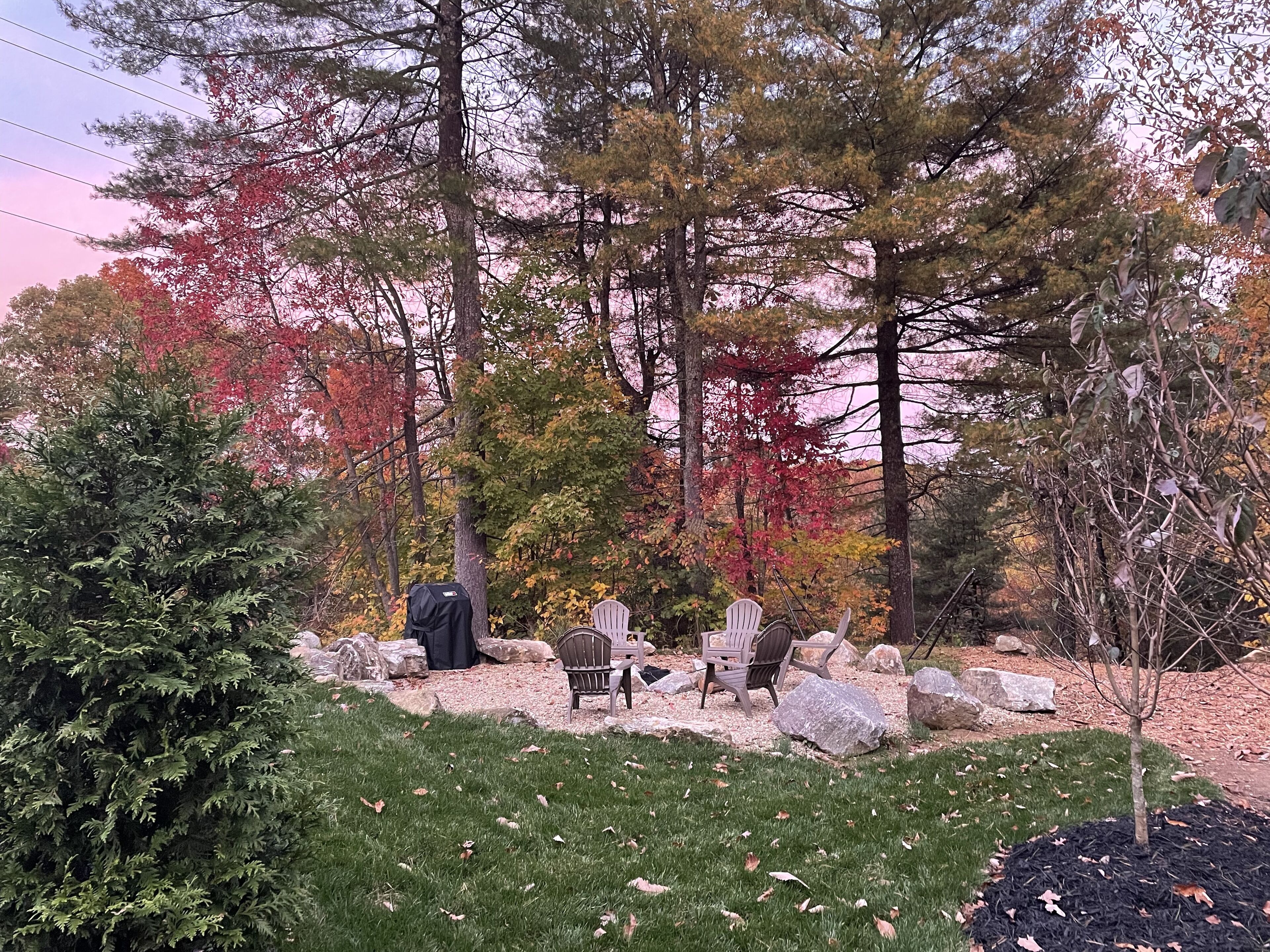 A garden with a seating area, rocks, and trees with autumn foliage.